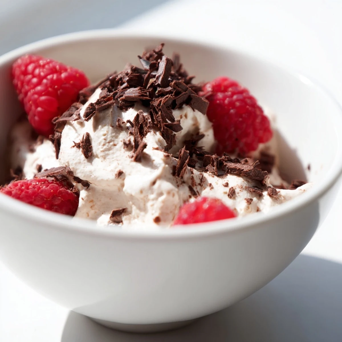 Four glass dessert cups of Chocolate Lunch Dessert mousse, topped with fresh raspberries, grated chocolate, and a dollop of whipped cream.