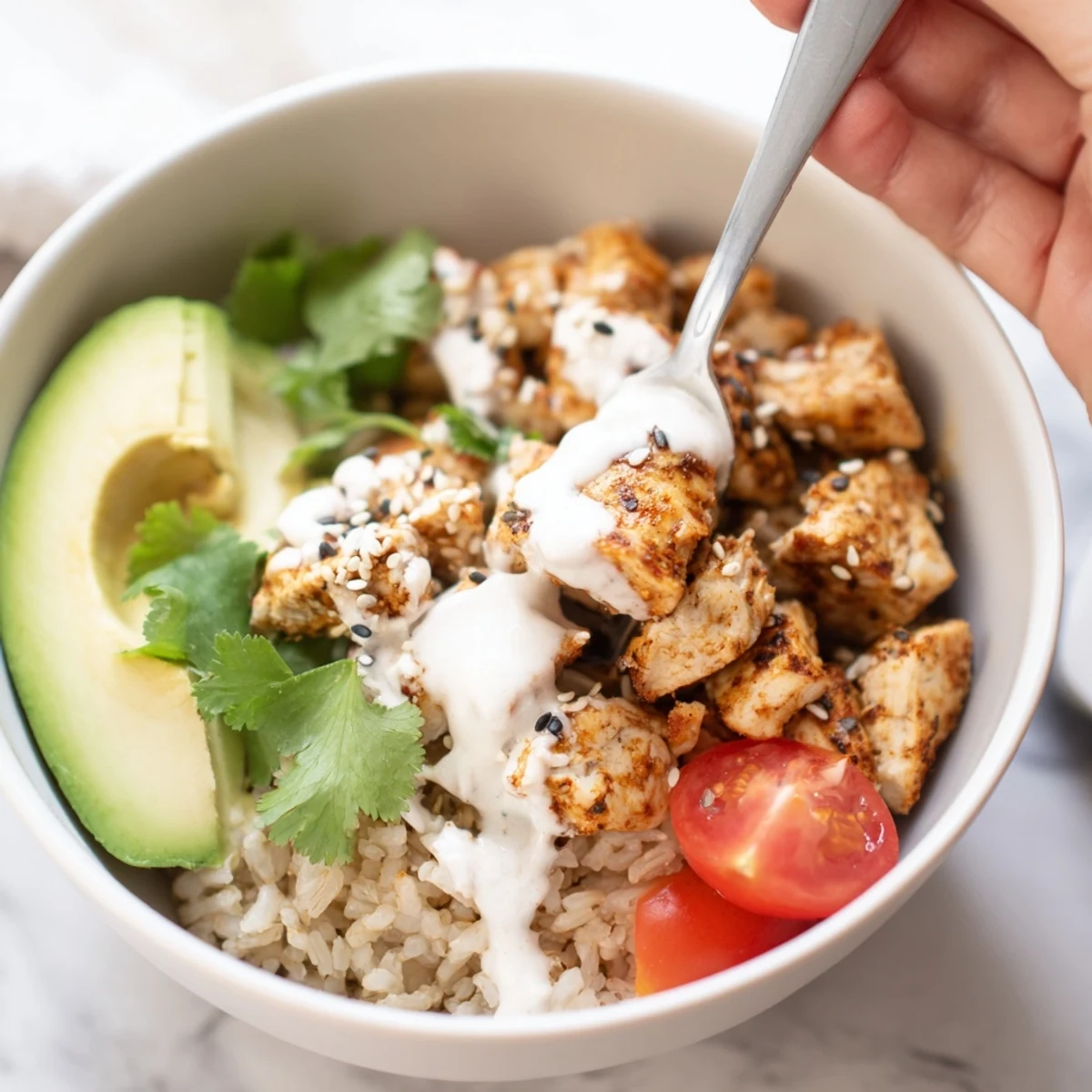 Vibrant Spicy Lunch Bowl with grilled chicken, brown rice, avocado, and colorful fresh vegetables, drizzled with creamy Sriracha lime sauce.