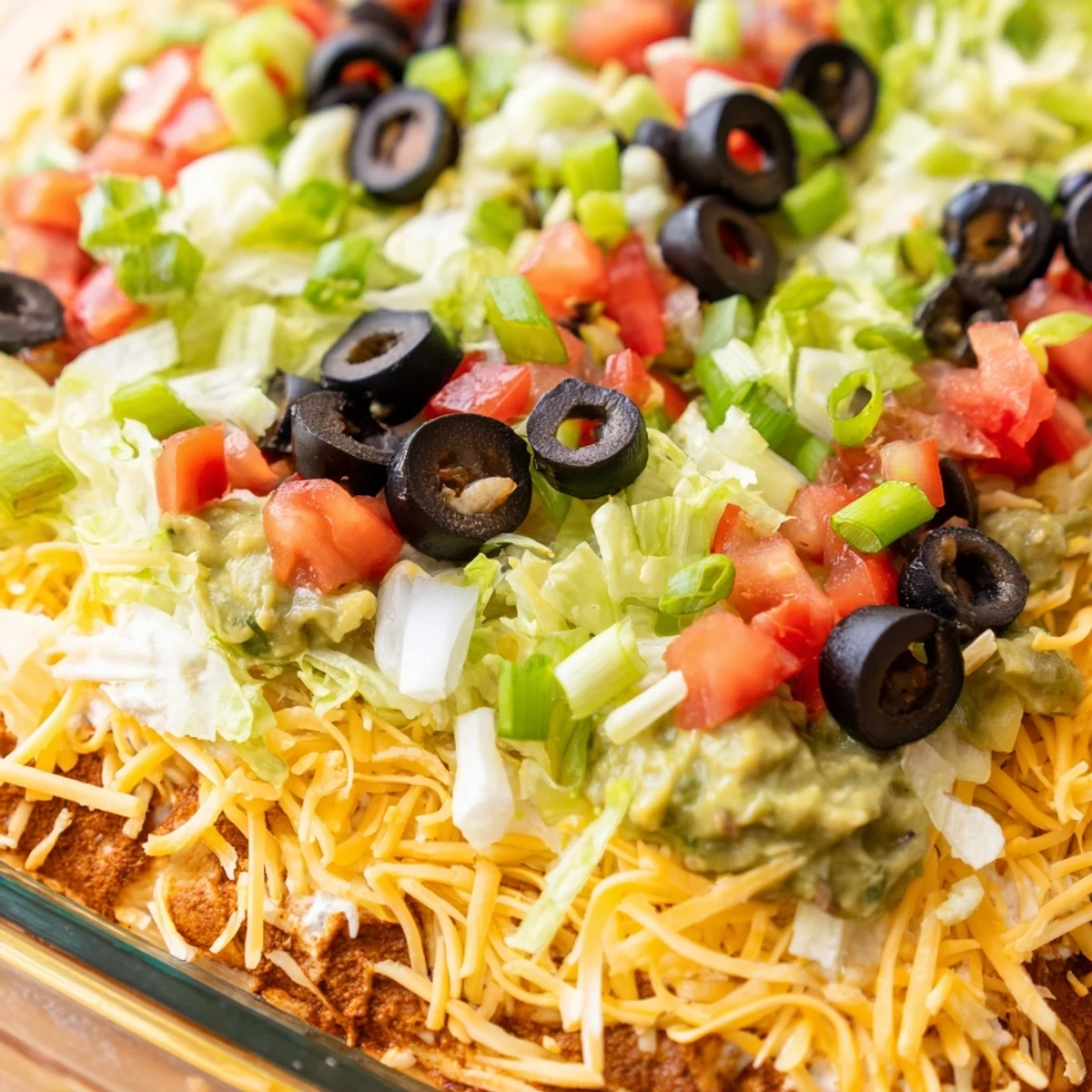 A colorful crowd-pleasing dip, garnished with olives and scallions, ready for game day scooping with sturdy tortilla chips.