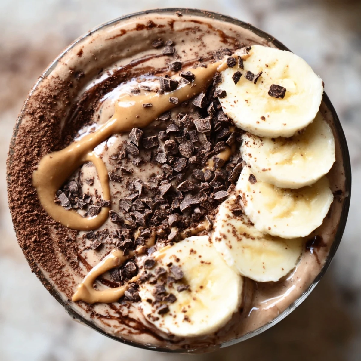 Two glasses of Chocolate Peanut Butter Smoothie with Banana sit beside fresh ingredients on a bright countertop.  