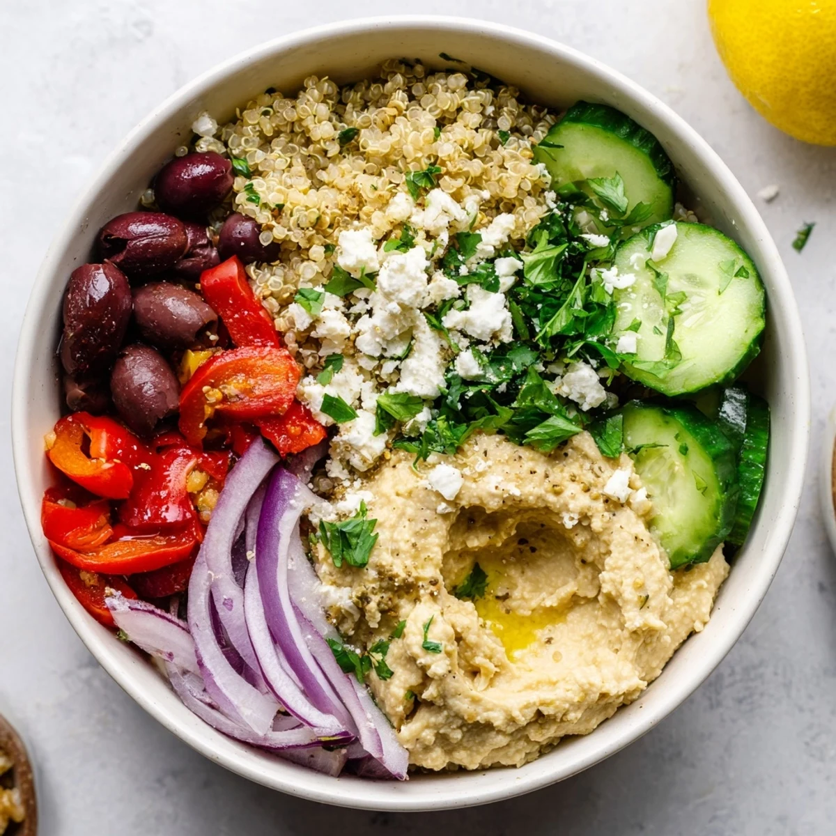 Fluffy quinoa topped with fresh vegetables, feta, olives, and a dollop of creamy hummus in a vibrant bowl.  