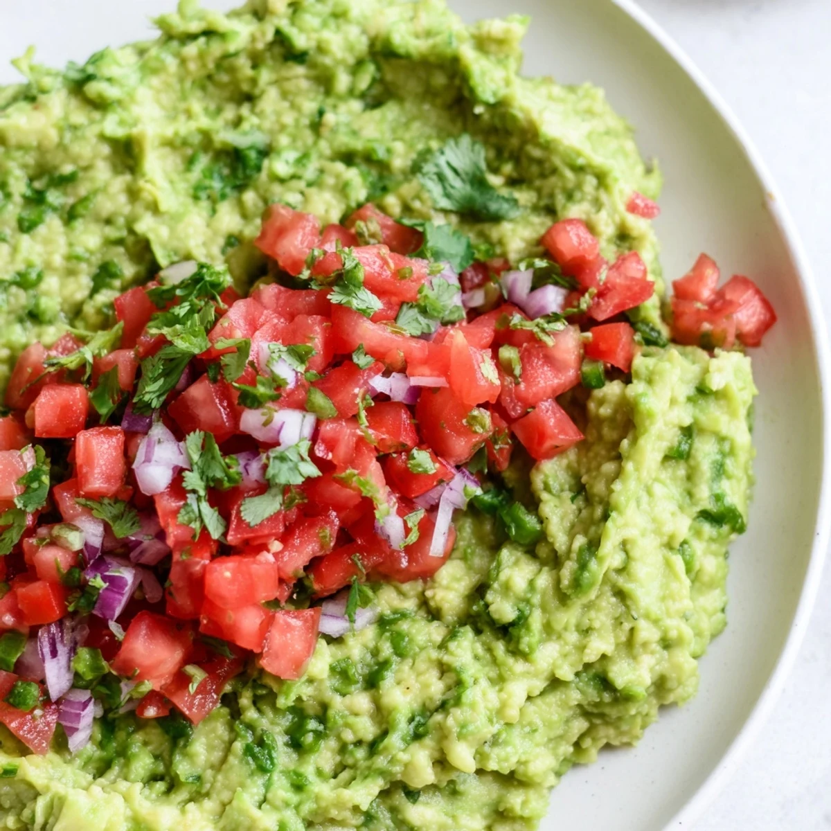 A colorful Super Bowl Guacamole with Pico de Gallo served alongside crunchy carrot sticks and celery for a lighter, veggie-friendly snack.