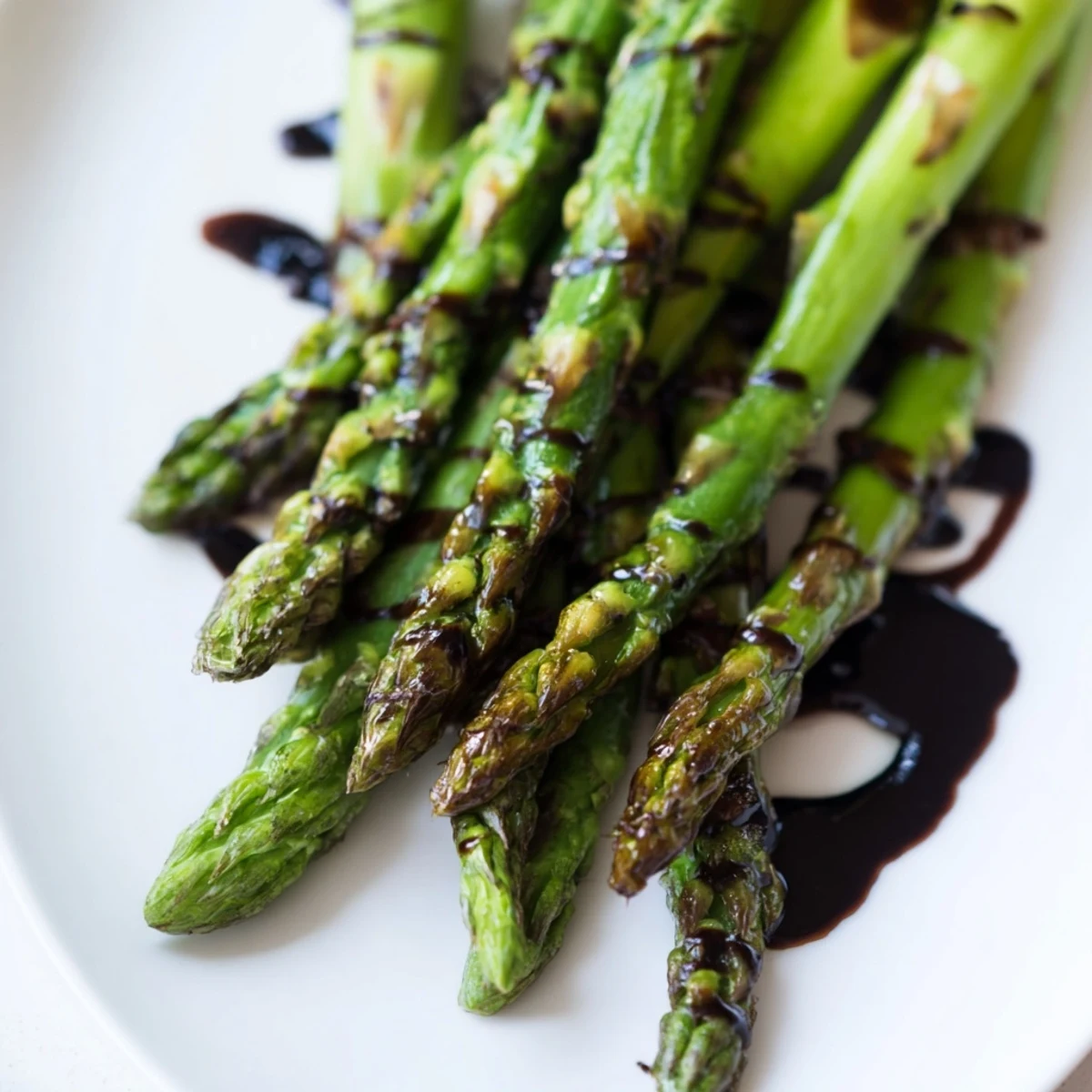 Tender roasted asparagus with balsamic glaze on a white plate, garnished with fresh thyme.