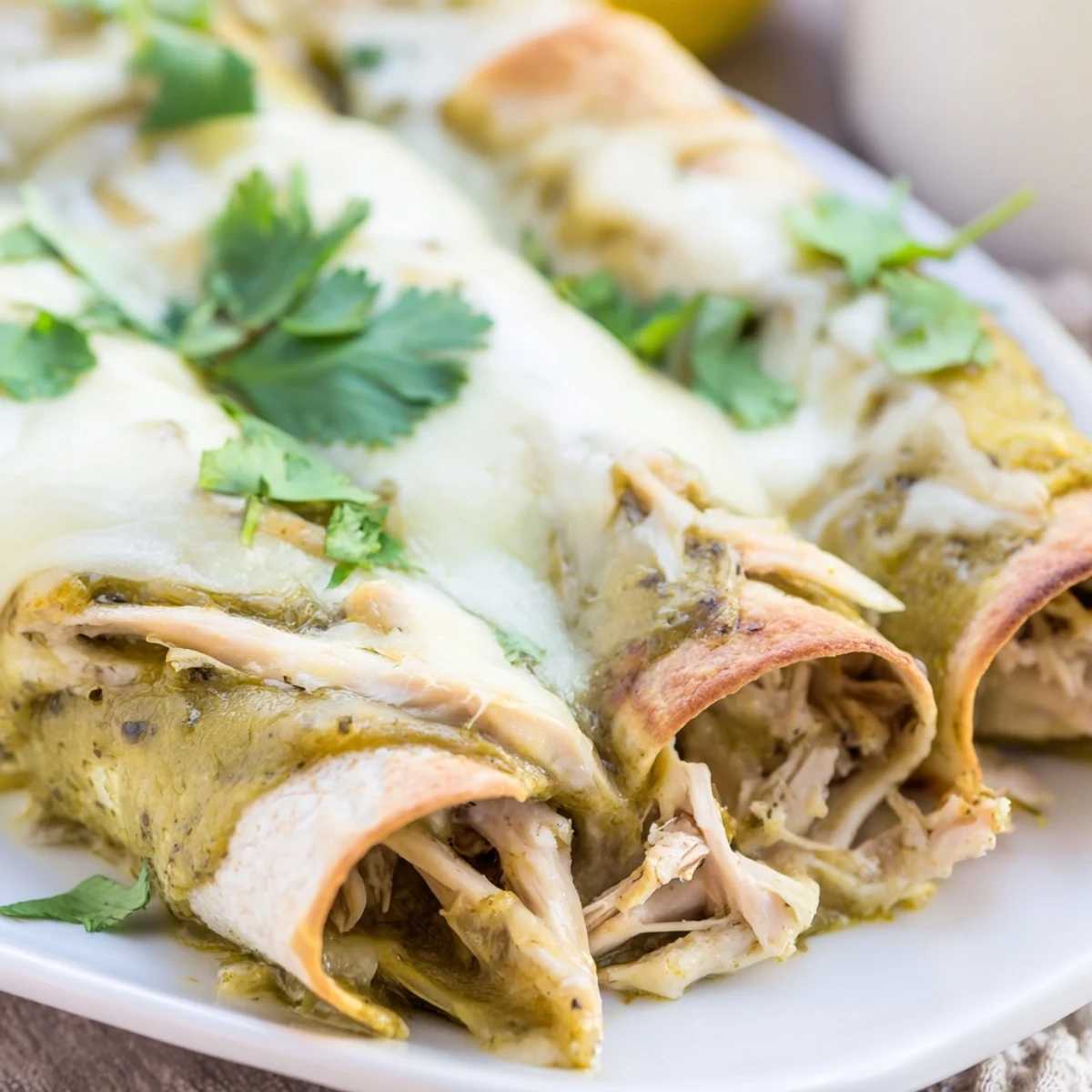 Golden Green Enchiladas With Chicken topped with sour cream and diced avocado, served alongside a lime wedge on a rustic plate.