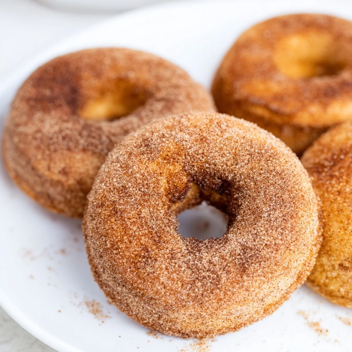 Glazing freshly baked Delicious Baked Cinnamon Sugar Donuts You Cant Resist with melted butter before dipping in cinnamon sugar coating.