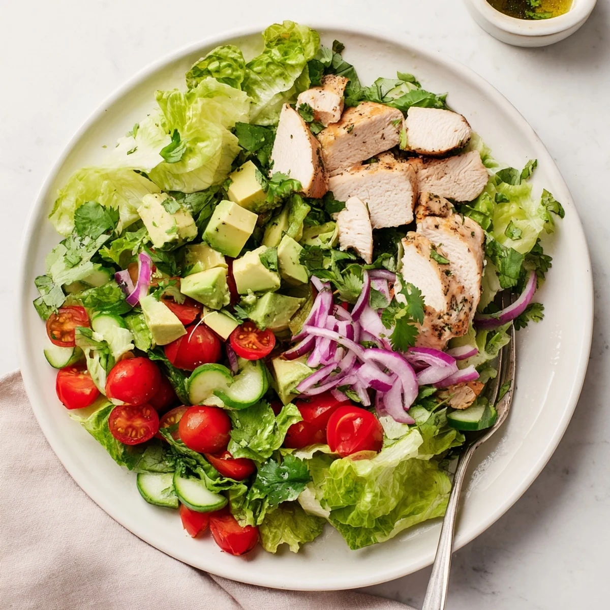 Grilled chicken slices atop avocado chicken salad with cherry tomatoes and mixed greens on a white platter.