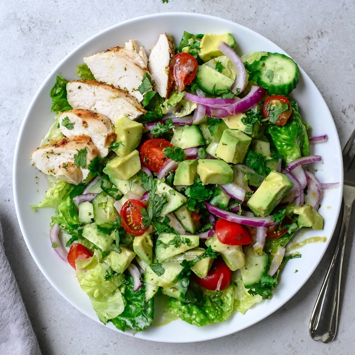 Close-up view of creamy avocado chicken salad in a bowl, featuring diced cucumber and juicy cherry tomatoes.