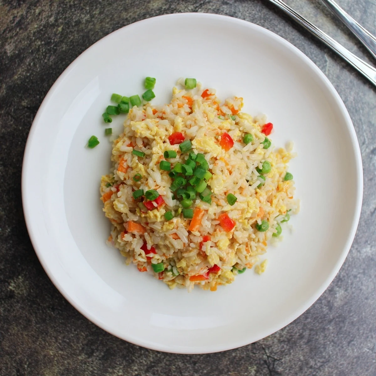 A close-up of vibrant Bang Bang Fried Rice in a white bowl, with colorful diced veggies and green onions garnish.