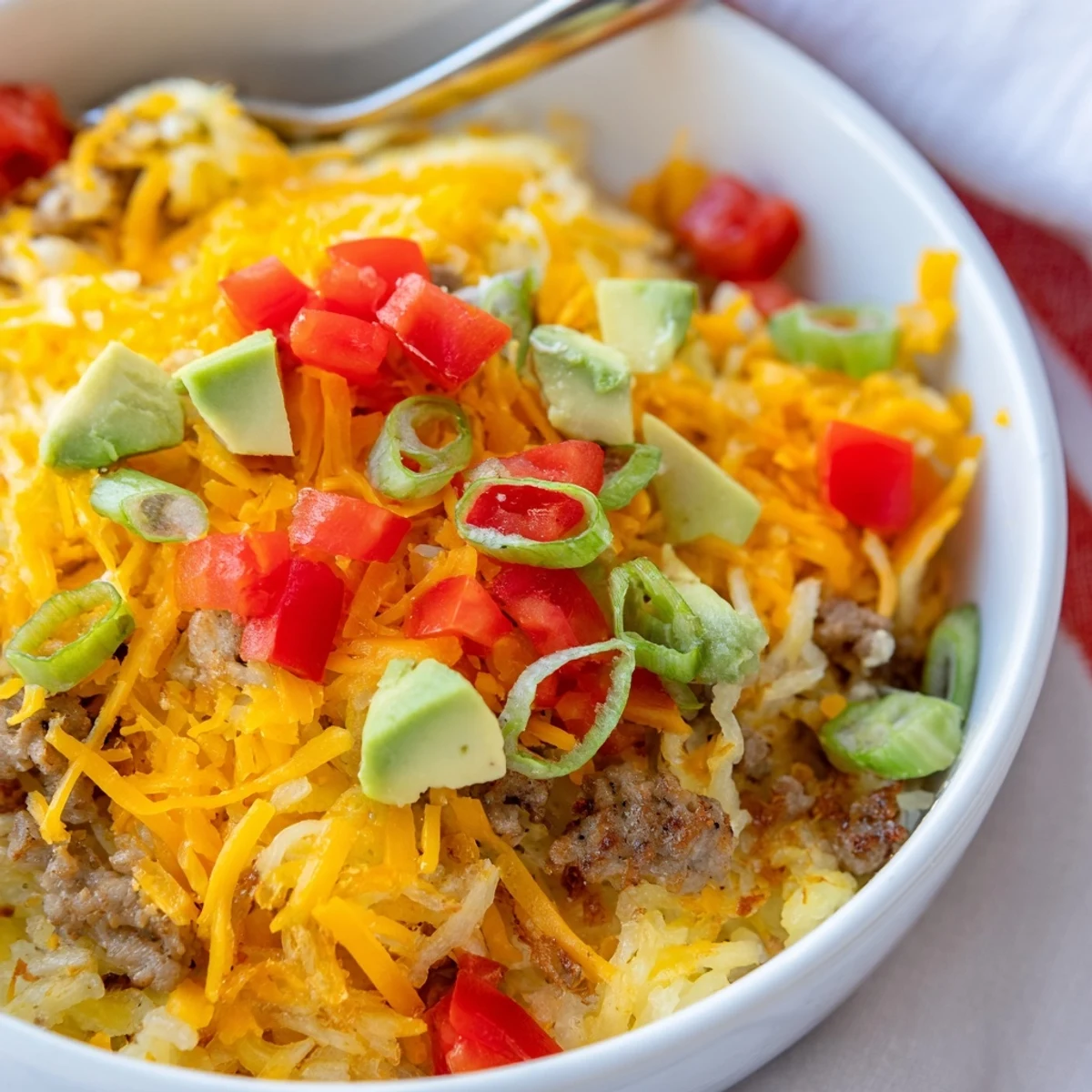 A close-up of Hash Brown Breakfast Bowls featuring crispy golden hash browns topped with fluffy scrambled eggs, savory sausage, and fresh avocado slices.