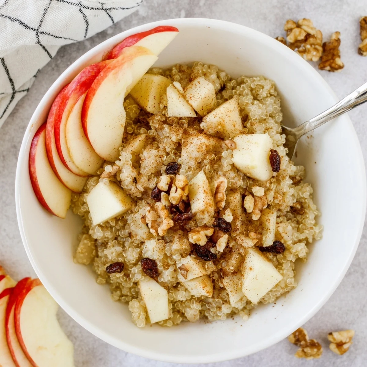 Vividly steaming Healthy Quinoa Apple Breakfast bowl, garnished with dried cranberries, extra apple slices, and a creamy swirl of milk.