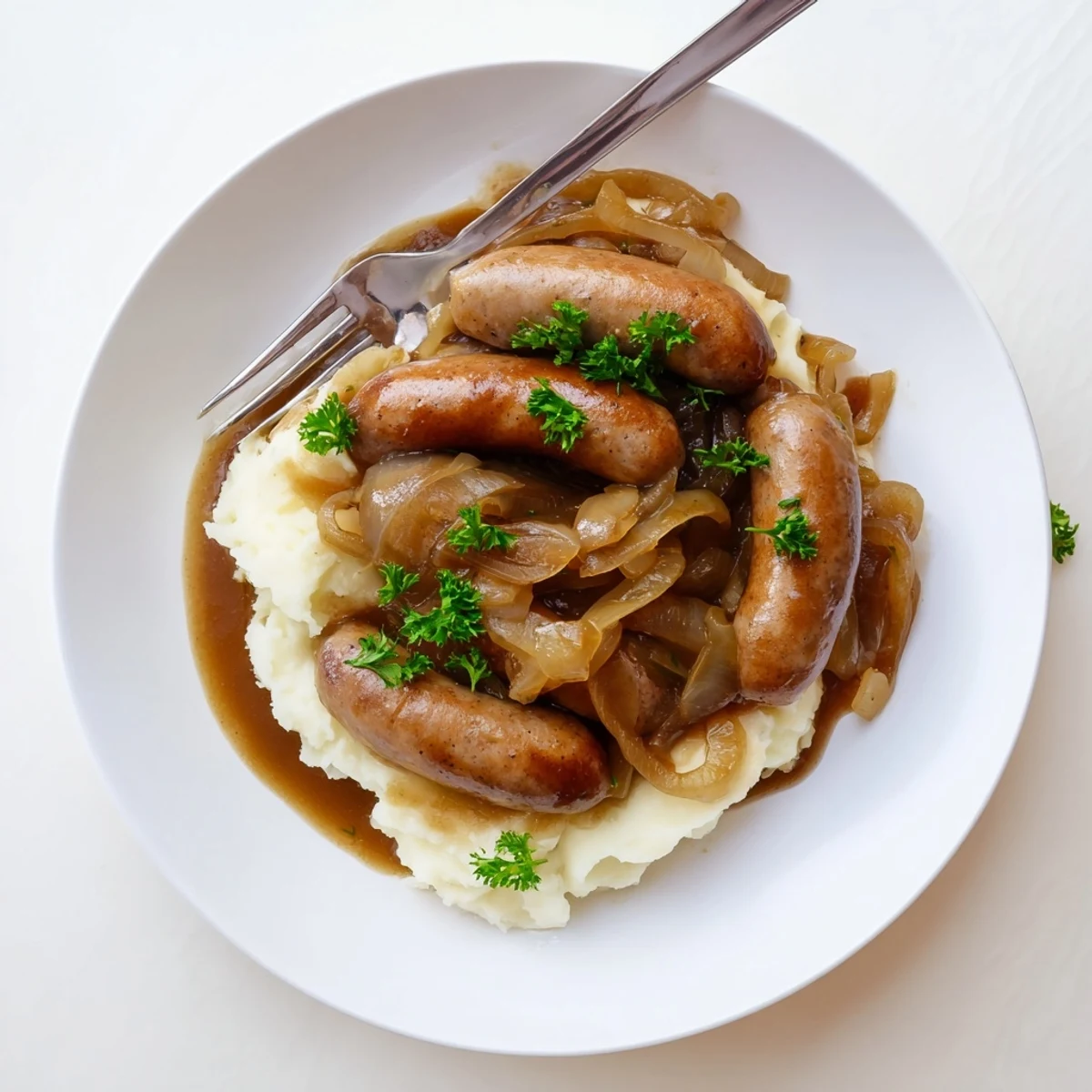 This comforting Sausages in Onion Gravy dish is served on a plate with a side of fresh green peas.  