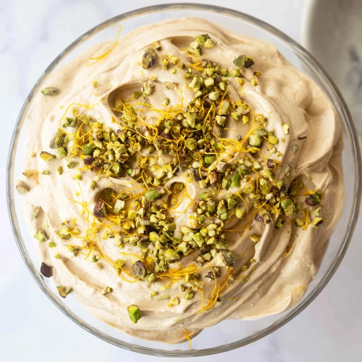 Airy Lebanese date orange blossom mousse dessert topped with green pistachios and citrus accents on white plate