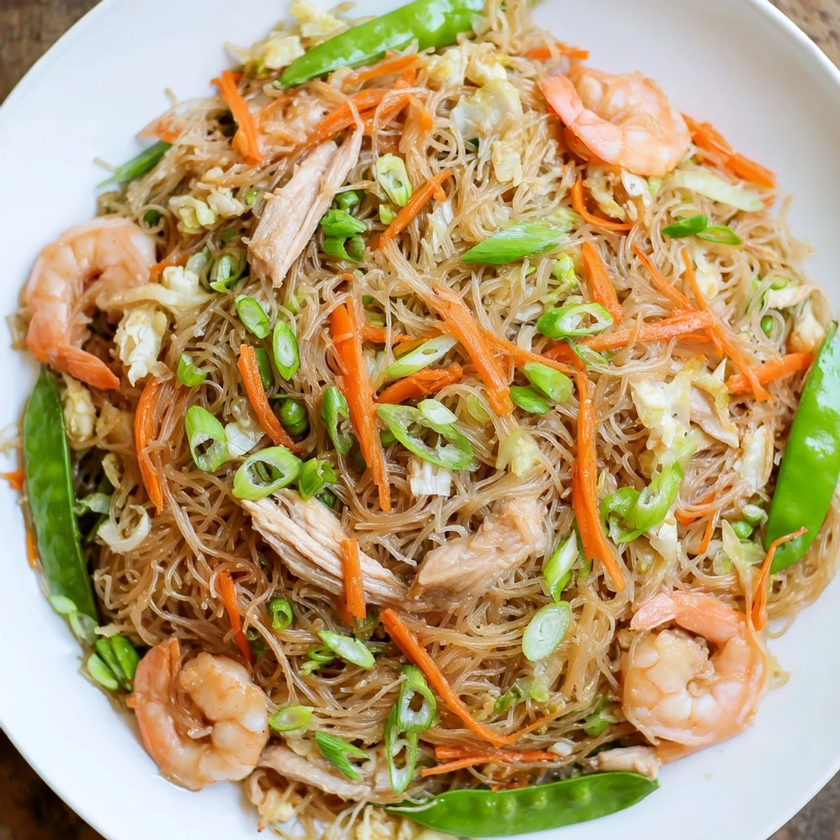 Steaming mound of Traditional Pancit Bihon rice noodles stir-fried with chicken, shrimp, and crisp vegetables in soy-based sauce