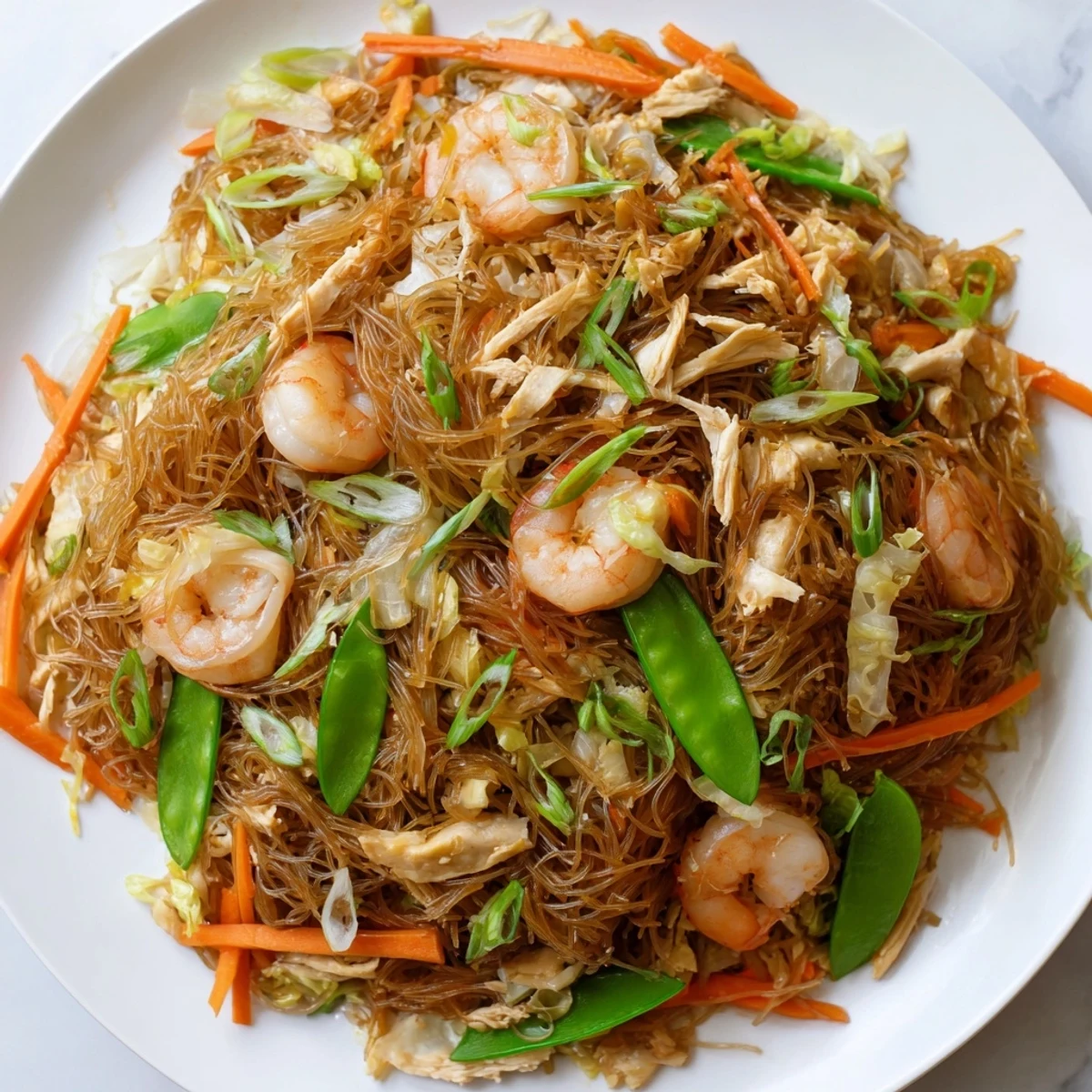 Golden plate of savory Traditional Pancit Bihon topped with tender chicken, plump shrimp, and colorful julienned vegetables