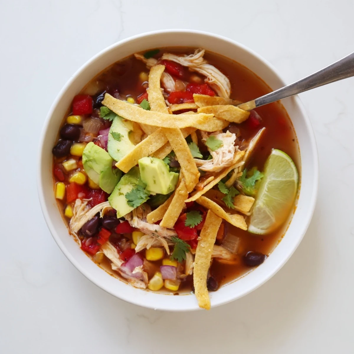 Creamy classic chicken tortilla soup garnished with zesty lime wedges, shredded cheese, and crisp tortilla strips for texture.