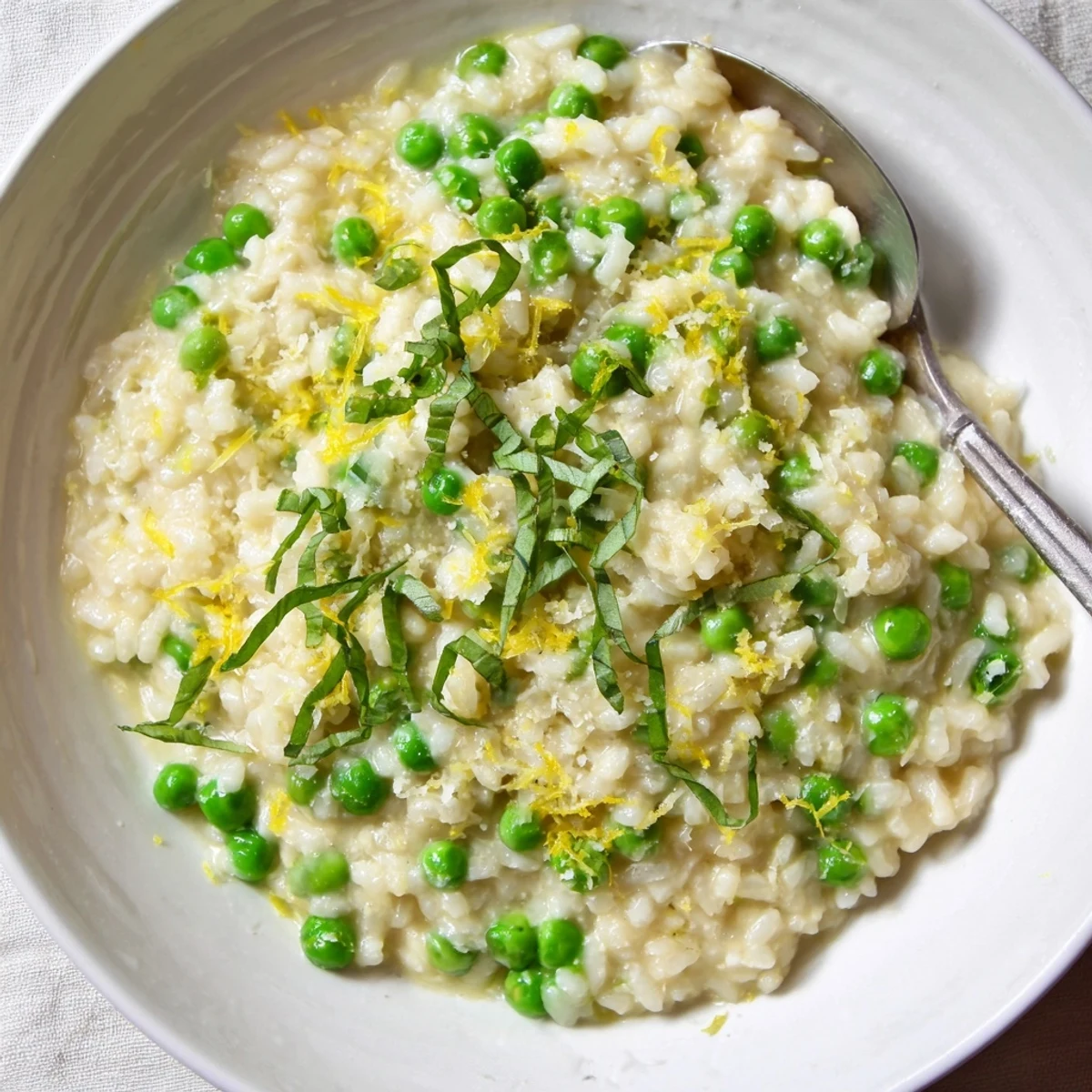 Creamy spring pea risotto topped with grated Parmesan and fresh green basil leaves