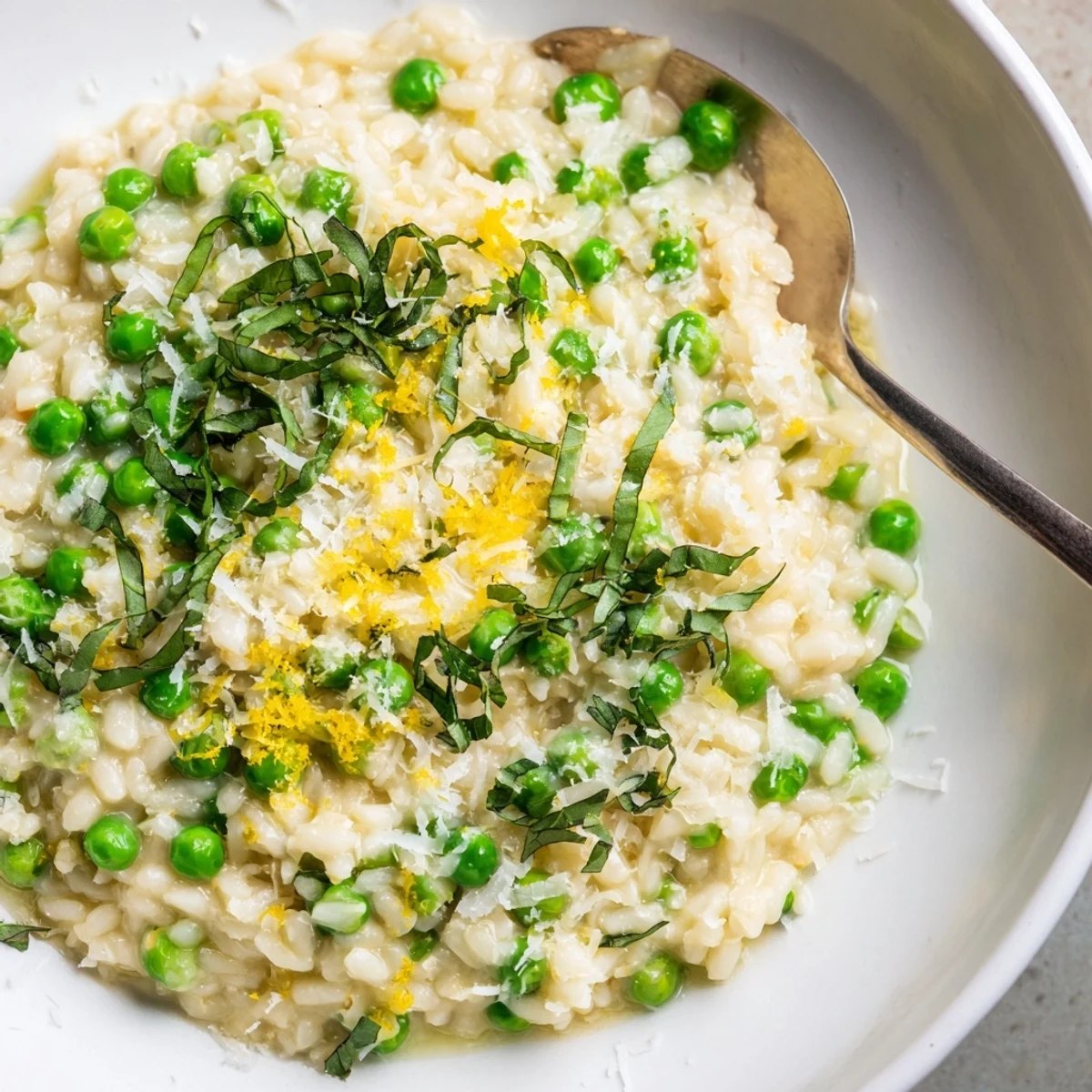 Bowl of vibrant pea risotto garnished with fresh basil and extra Parmesan cheese
