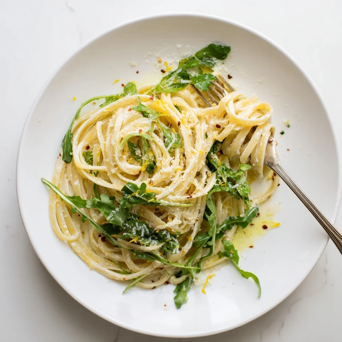 Twirled spaghetti coated in tangy lemon ricotta sauce atop peppery arugula leaves