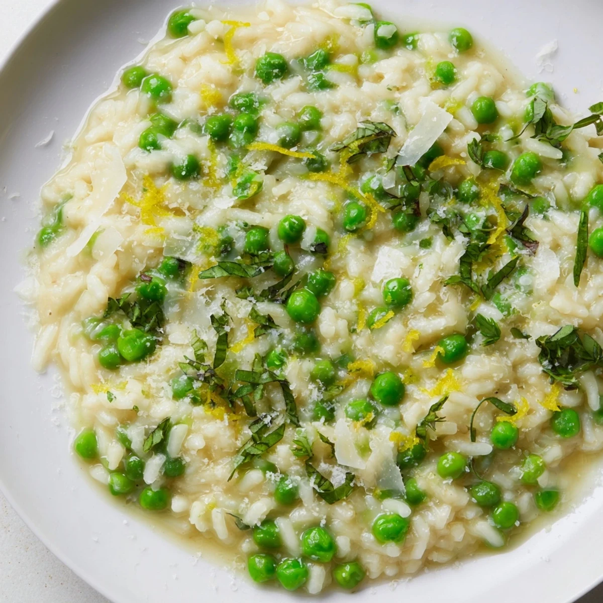 Creamy spring pea risotto topped with freshly grated Parmesan and vibrant green herbs in a shallow white bowl