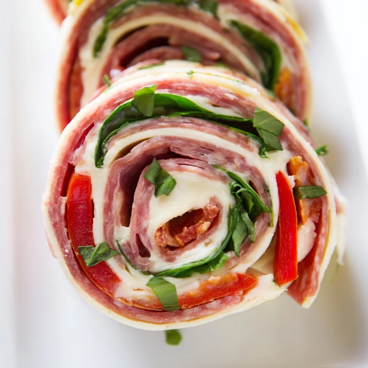 Fresh Italian pinwheels arranged on a serving platter with cream cheese spread and herb garnish