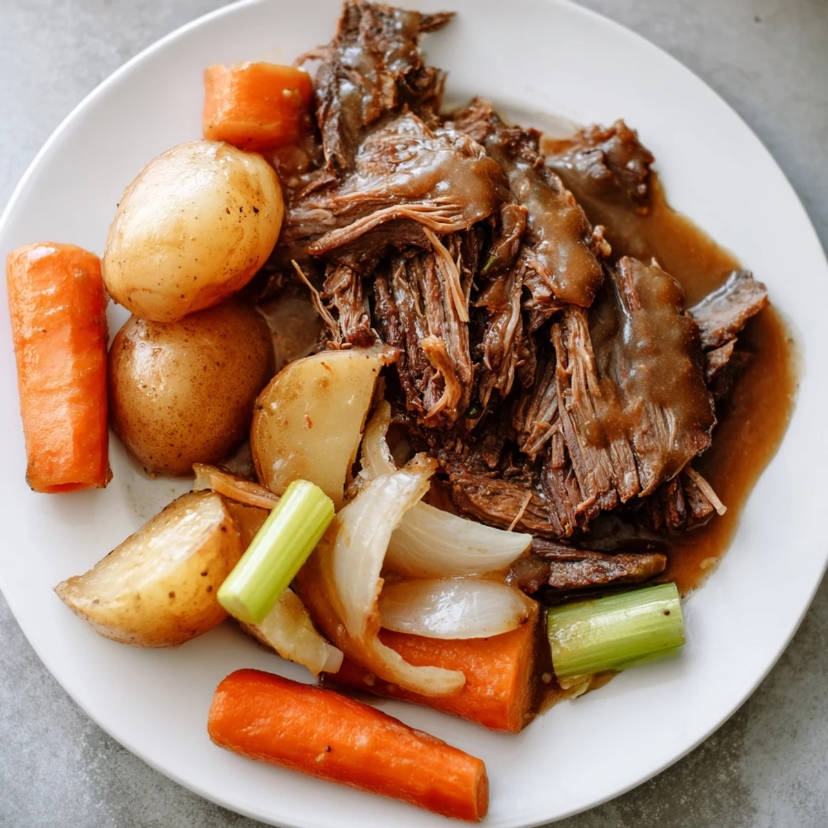 Fork-tender Southern style pot roast nestled alongside roasted vegetables and smothered in savory beef gravy