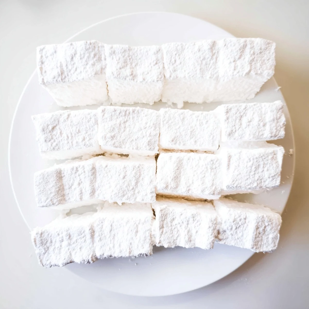 Fluffy white homemade marshmallows dusted with powdered sugar on a wooden cutting board