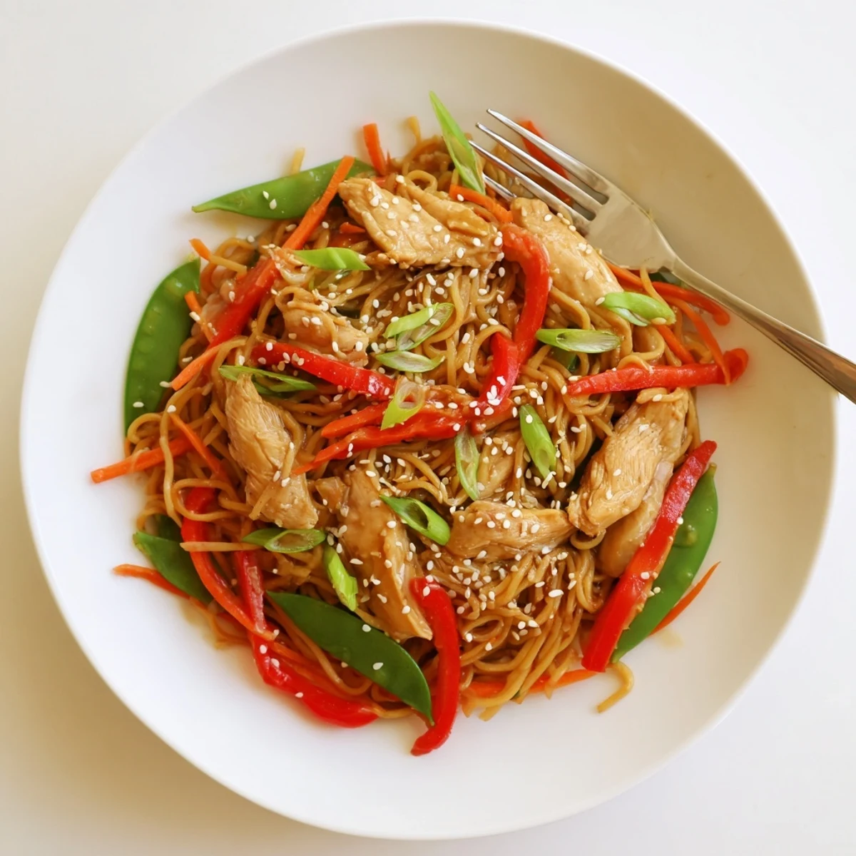 Glossy sticky garlic chicken noodles with tender meat and colorful crisp vegetables in a bowl