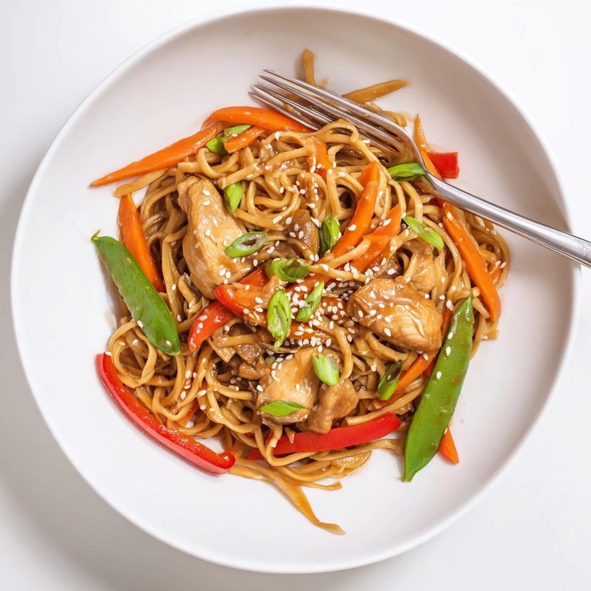 Steamy bowl of sticky garlic chicken noodles tossed with peppers, carrots, and snap peas