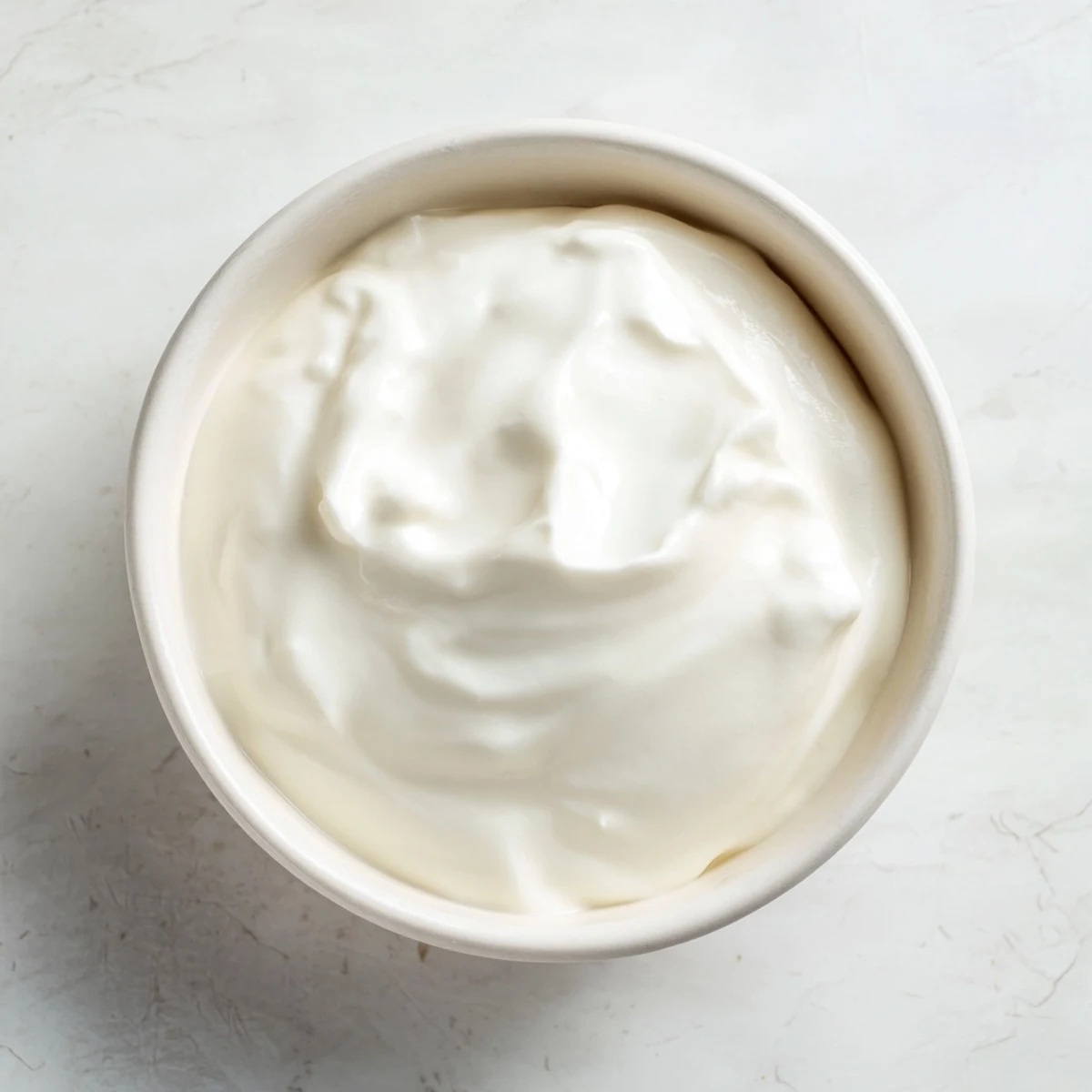 Rich velvety Greek yogurt strained through cheesecloth in a sieve over a deep bowl