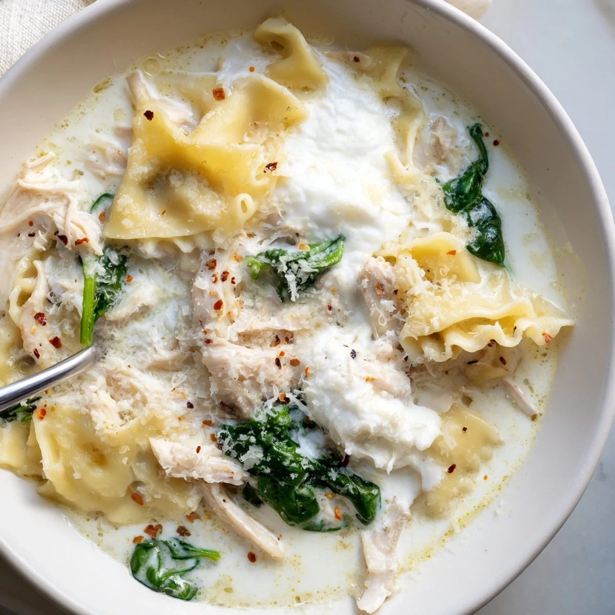 A steaming ladleful of white lasagna soup with tender broken noodles spinach and Parmesan