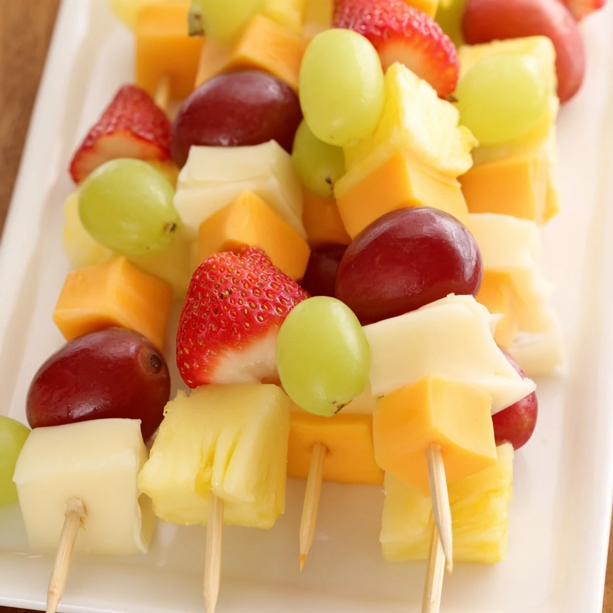 Fruit and cheese kabobs arranged on a platter with grapes, strawberries, pineapple, and cheddar cubes