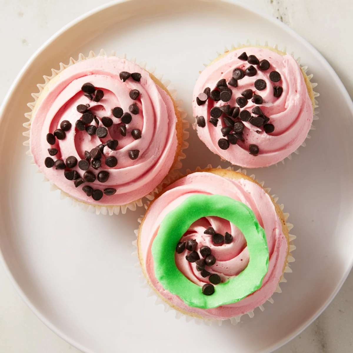 Moist vanilla watermelon cupcakes topped with creamy pink frosting and mini chocolate chip seeds