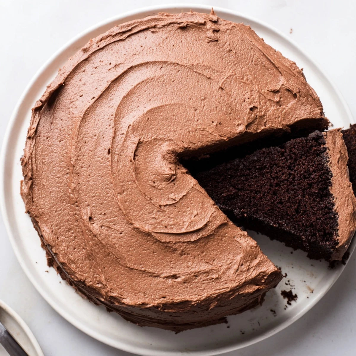Chocolate cake recipe on wire rack cooling, velvety frosting being spread  