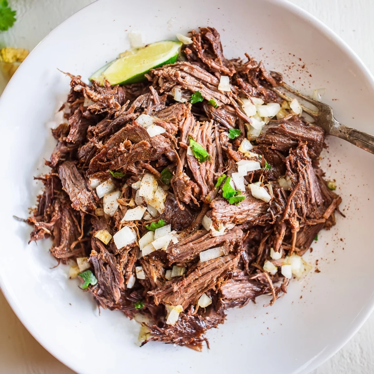 Shredded Slow Cooker Beef Barbacoa with cilantro, diced onion, lime wedges
