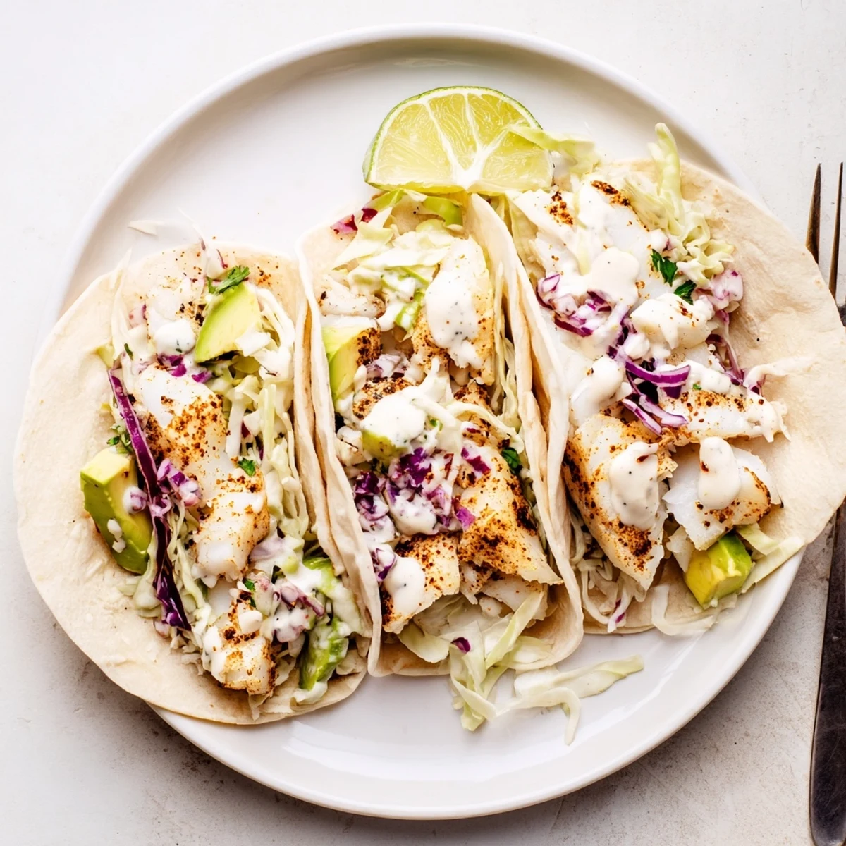 Baked Cod Fish Tacos with Creamy Cilantro Lime Sauce, drizzled over flaky fish
