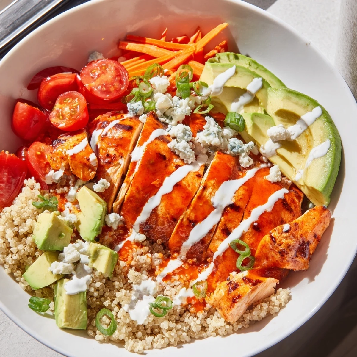 Juicy buffalo chicken grain bowl topped with fresh avocado, shredded carrots, and blue cheese