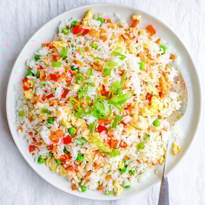 Bang Bang Fried Rice is served steaming hot on a dark plate, with a drizzle of creamy chili sauce visible.