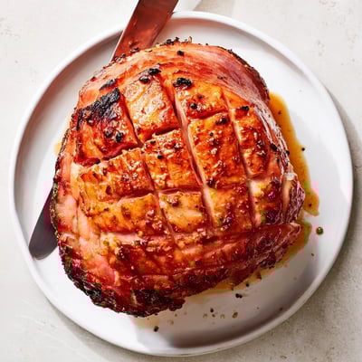 Whole cloves stud the scored crust of this Baked Ham with Maple Dijon Glaze, resting on a wooden cutting board next to a glaze-coated brush.